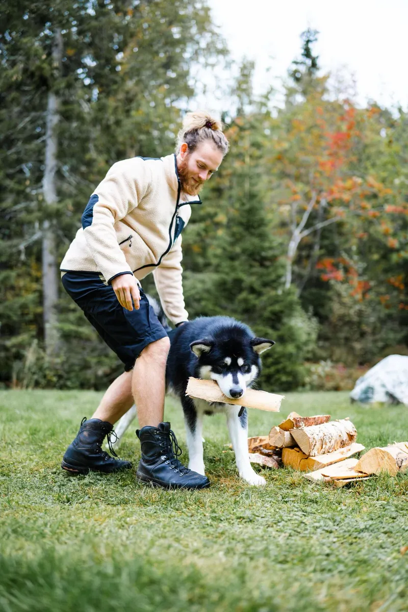 Un homme joue avec son husky sur une pelouse en forêt