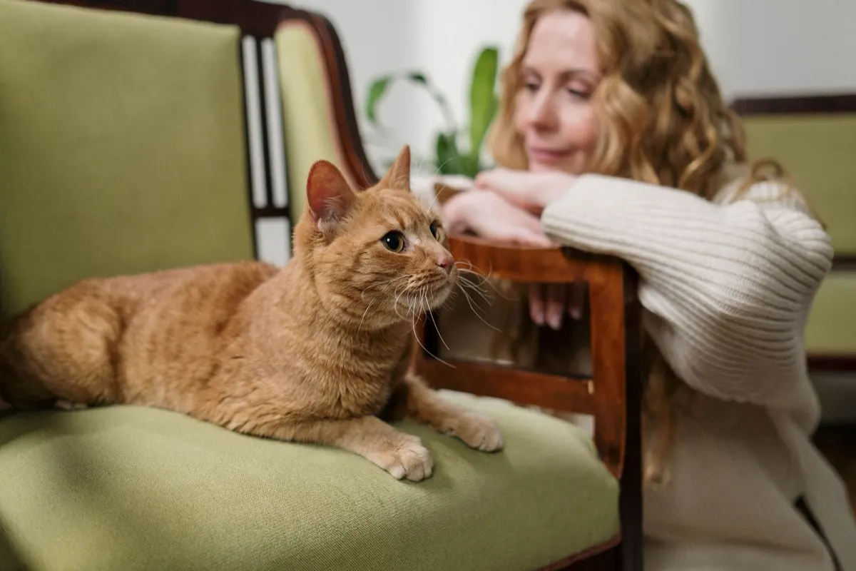 Une femme souriante assise près de son chat roux sur un fauteuil